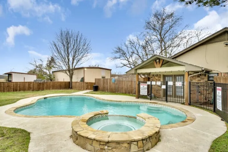 The fenced swimming pool and clubhouse under a blue sky at Waggin' Tail Ranch RV Resort near DFW