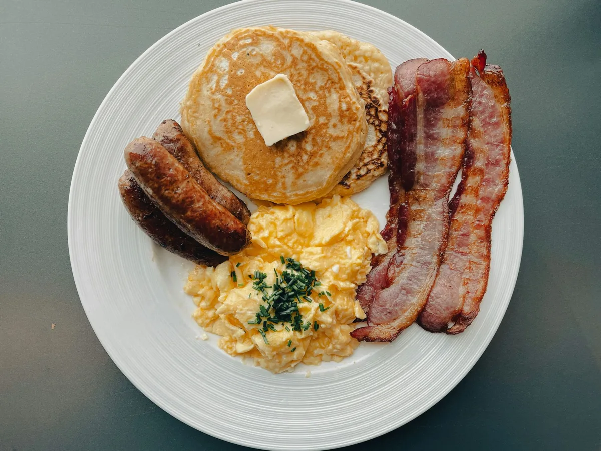 Breakfast plate of buttermilk pancakes with butter, scrambled eggs, bacon, and sausage