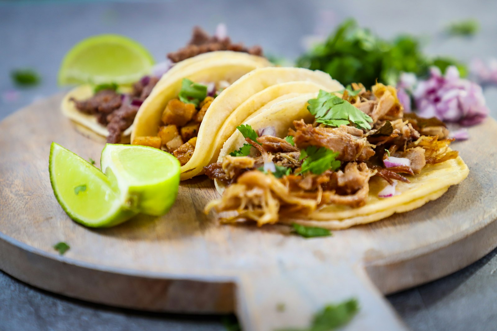 Three street-style tacos with lime on a wooden board