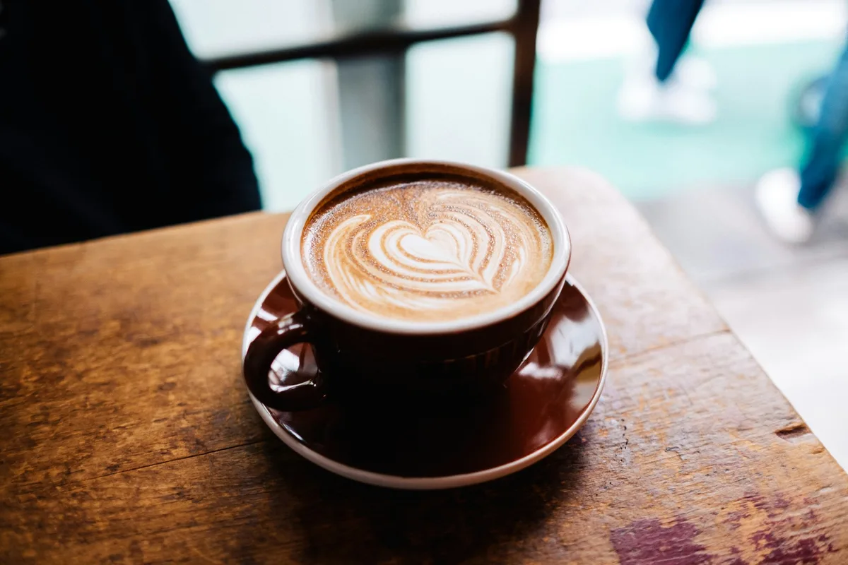 Latte with heart-shaped foam art in a brown cup on a wooden table