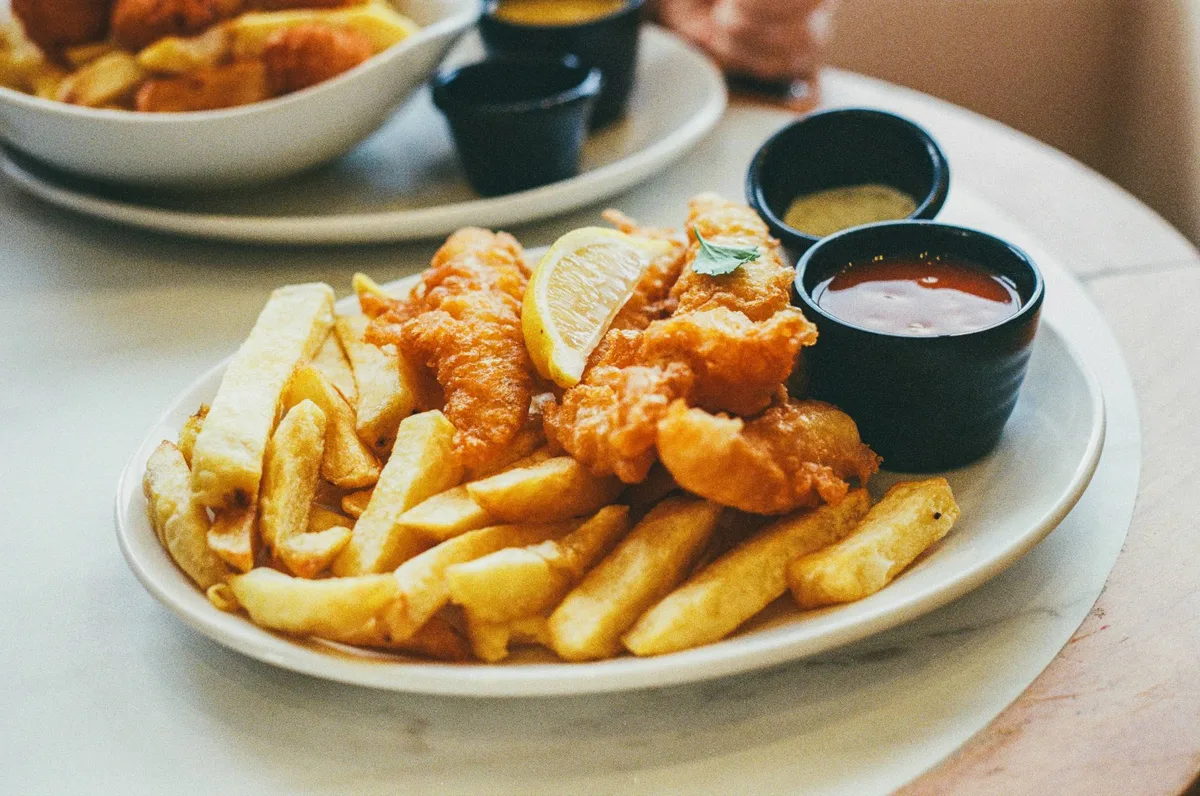 Plate of battered fish and thick-cut fries with lemon and dipping sauces