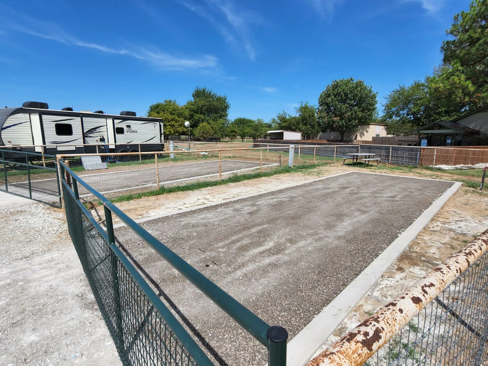 An empty fully fenced RV site with green gate and concrete pads waiting for a weekend guest at Waggin' Tail Ranch RV Resort in Pilot Point, TX